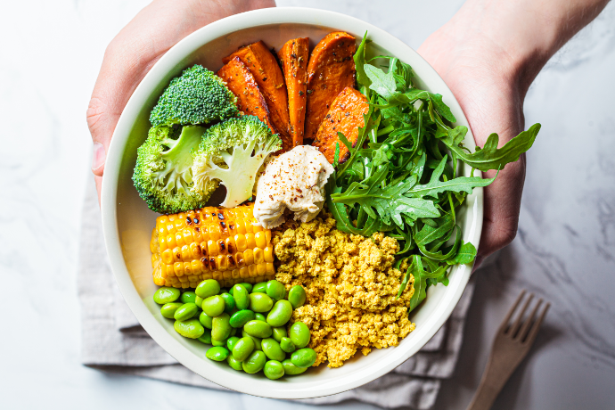 A person holding a bowl filled with nutritious foods included in a healthy eating plan to manage cholesterol.